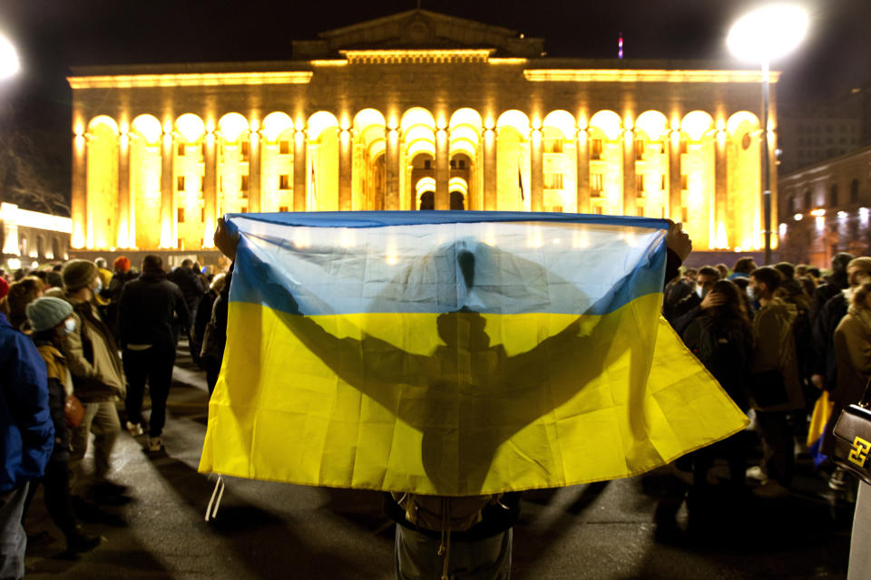 A demonstrator holds a Ukrainian national flag in front of the Georgian Parliament during an action against Russia's attack on Ukraine in Tbilisi, Georgia, Tuesday, March 1, 2022. Russian shelling pounded civilian targets in Ukraine's second-largest city again, and a 40-mile convoy of tanks and other vehicles threatened the capital. (AP Photo/Shakh Aivazov)