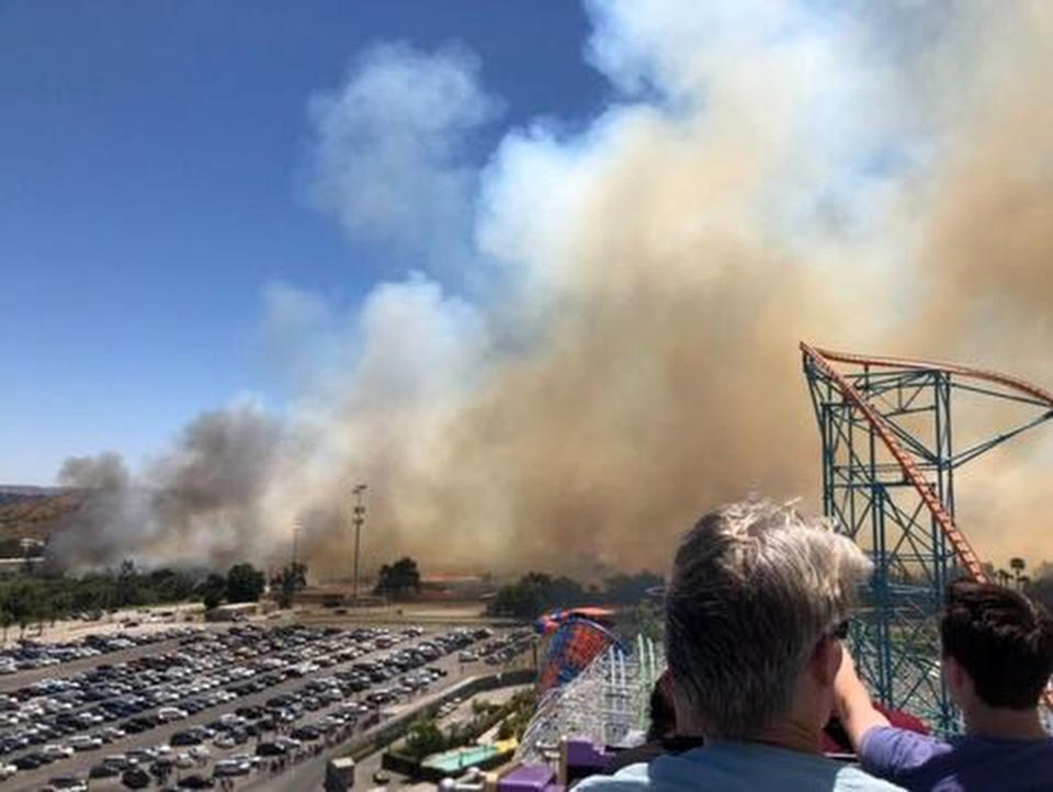 This photo provided by Ryan Reede shows smoke from a fast-moving brush fire that Reede took as he was riding on a roller coaster at Six Flags in Valencia, north of Los Angeles. The brush fire erupted near the huge amusement and water park in Southern California on Sunday, sending hundreds of visitors to the exit to escape clouds of smoke and ash before fire officials asked them to stay put while they worked to contain the blaze. (Ryan Reede via AP)