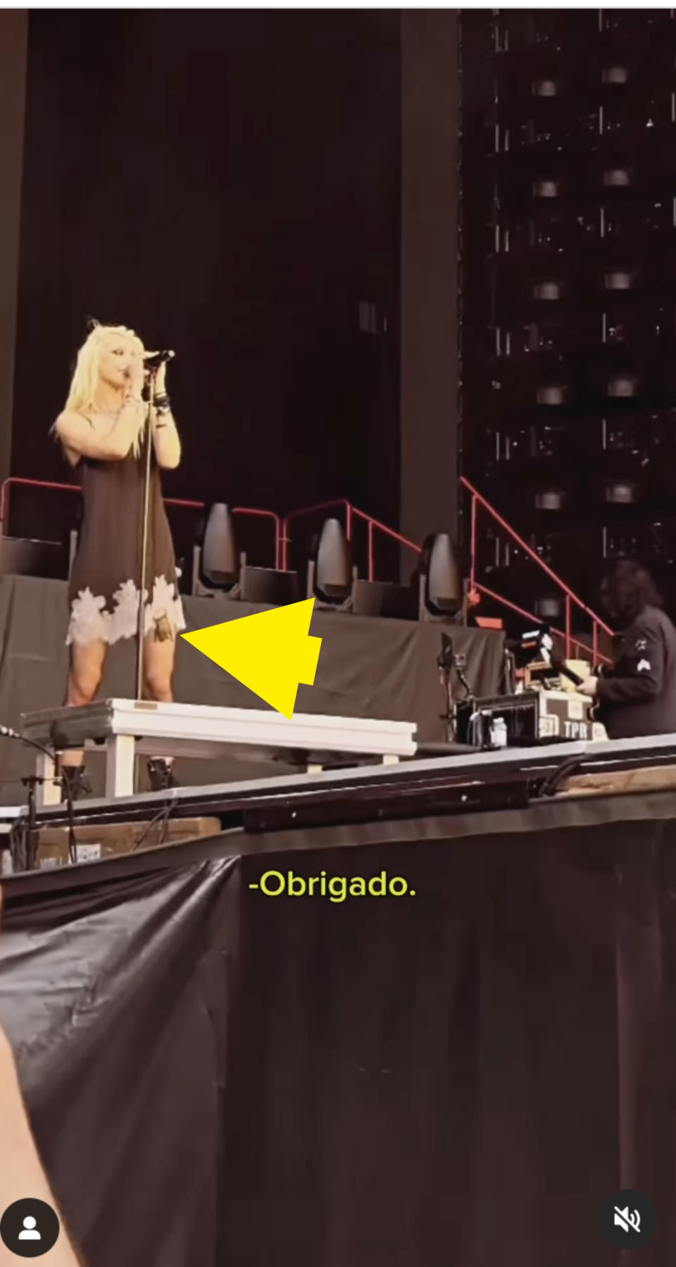 Taylor Momsen performs on stage, dressed in a stylish dress with intricate patterns. The word "Obrigado" is displayed in yellow text below her