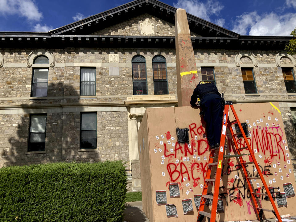 A police officer surveys graffiti after two dozen advocates for Native American communities gathered in downtown Santa Fe, N.M., Monday, Oct. 10, 2022, when most government offices were closed in commemoration of Indigenous Peoples Day, a state holiday. Demonstrations left paint splashed across a monument to 19th century trapper-turned-soldier Kit Carson, outside a federal courthouse. Carson is revered and reviled as a pivotal figure in the settlement of the American West and deadly military campaigns against Native Americans including the Navajo. Demonstrators chanted, "This is Native land," and "1680," in reference to the year of the Pueblo Indian Revolt that drove Spanish settlers out of the region for a dozen years. Signs and banners also called for justice concerning missing and murdered Indigenous women. (AP Photo/Morgan Lee)