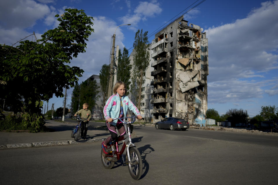 A girl rides a bicycle in front of houses ruined by shelling in Borodyanka, Ukraine, Tuesday, May 24, 2022. (AP Photo/Natacha Pisarenko)