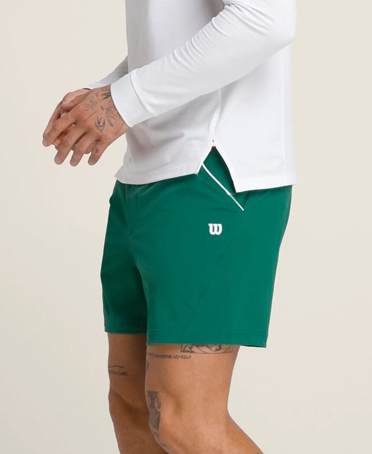 model wearing green tennis shorts and white long sleeve tennis shirt