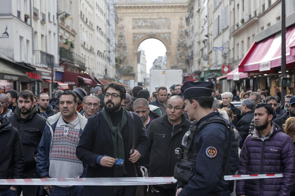 Transeúntes se agolpan detrás de la cinta que rodea la escena donde se produjo un tiroteo en el centro de París, viernes 23 de diciembre de 2022. (AP Foto/Lewis Joly)