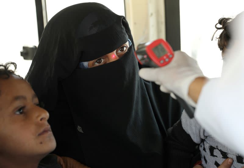 FILE PHOTO: A health worker takes the temperature of a woman riding a taxi van, amid concerns of the spread of the coronavirus disease (COVID-19), at the main entrance of Sanaa, Yemen
