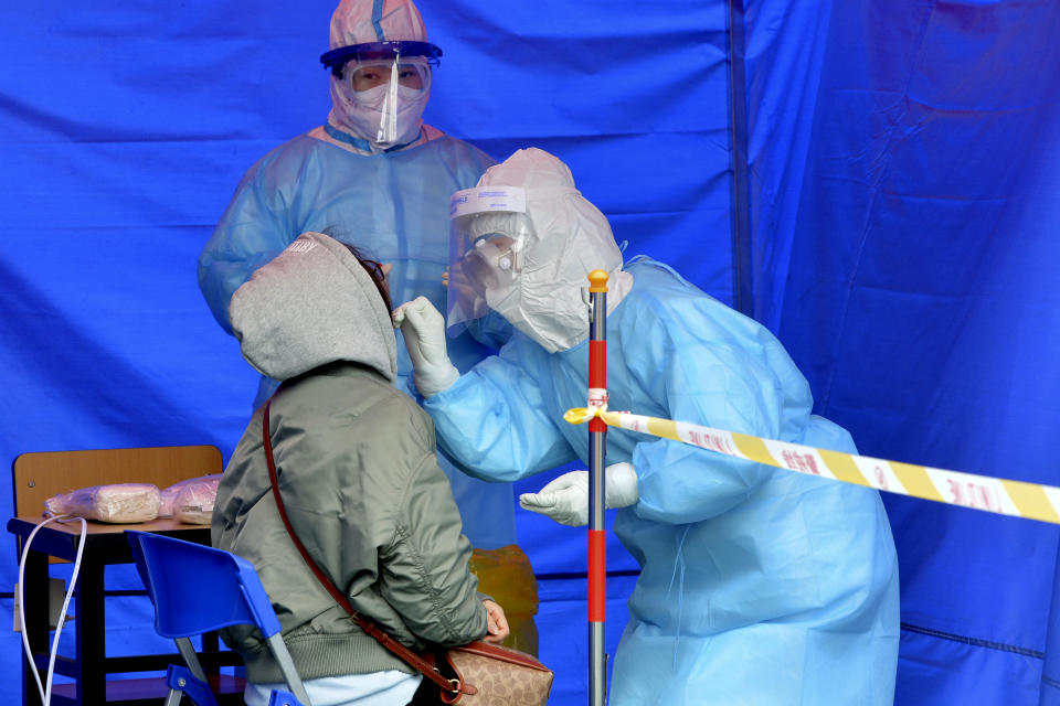 Workers wearing protective suits take a throat swab from a person at a COVID-19 testing site in Tianjin, China, Saturday, Nov. 21, 2020. China is starting mass testing on 3 million people in a section of the northern city of Tianjin and has tested several thousand others in a hospital in Shanghai after the discovery of a pair of cases there. (Chinatopix via AP)