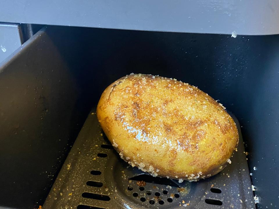 The inside of an air-fryer basket containing one seasoned potato