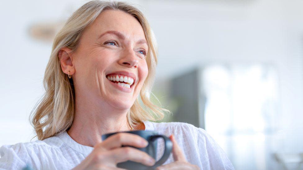 A woman smiling and holding a cup 