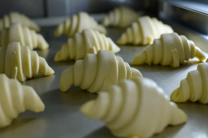 Unbaked croissants arranged on a baking tray in a commercial kitchen, ready for baking