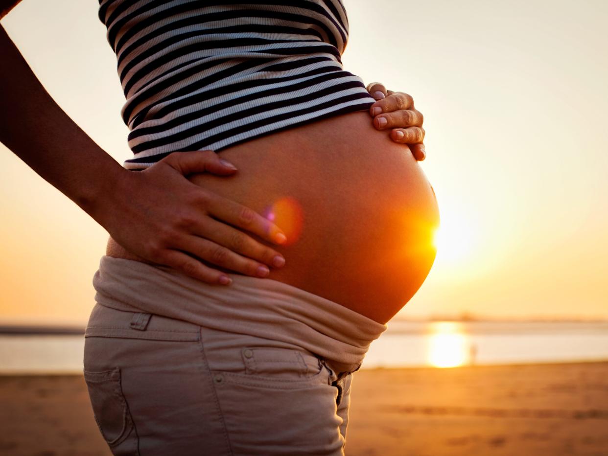 A pregnant woman holding her belly on the beach at sunset