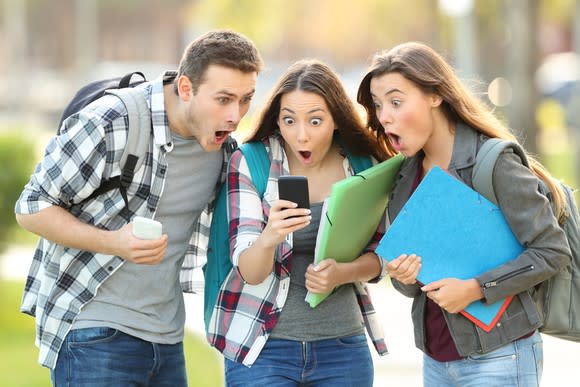 Three young people watch a video on a smartphone.