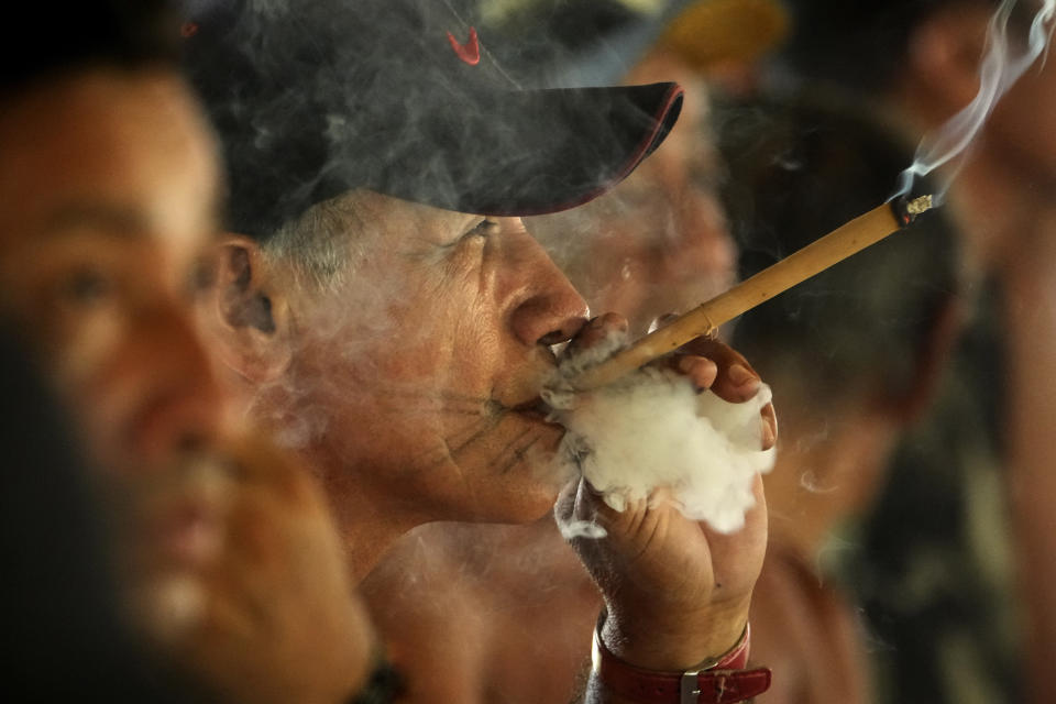 El jefe Sergio Muti Tembñe fuma un cigarro durante el rito de madurez Wyra'whaw, en el centro ritual Ramada, en la aldea Tenetehar Wa Tembe, en la tierra indígena Alto Río Guamá, en el estado de Pará, Brasil, el 10 de junio de 2023. (AP Foto/Eraldo Peres)