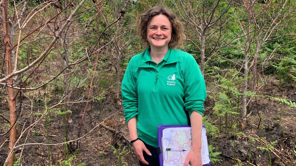 Leoni Dawson smiling among burnt trees, holding a clipboard