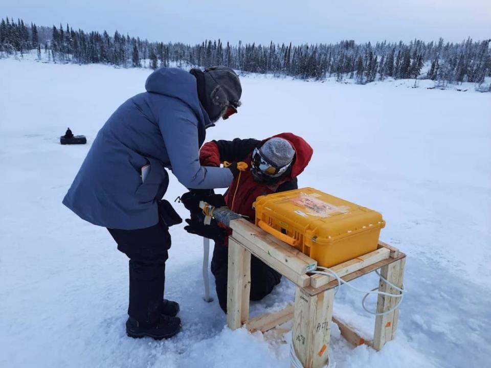 Homa Kheyrollah Pour (left) and Arash Rafat (right) install a snow and ice mass balance apparatuses — or SIMBA for short — on Ryan Lake in the N.W.T. The researchers from Wilfrid Laurier University leaned into the device's acronym and named this device Simba. Another one, located at Landing Lake, is called Mufasa.  (Alex MacLean/ReSEC Lab - image credit)