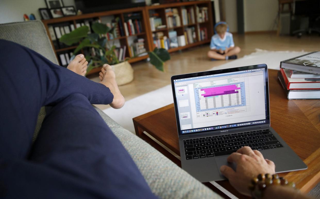 A man works from home on a MacBook Pro laptop as a child wearing headphones sits beyond - Stefan Wermuth/Bloomberg