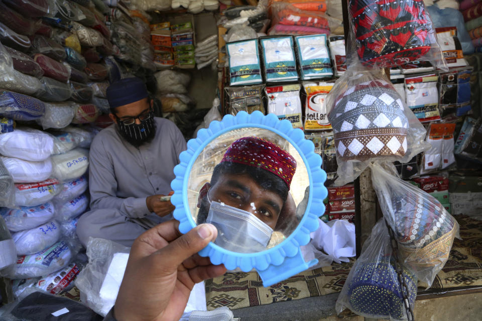 FILE - In this Thursday, April 8, 2021, file photo, a man tries on a traditional cap in preparation for the upcoming Muslim fasting month of Ramadan, in Peshawar, Pakistan. Muslims are facing their second Ramadan in the shadow of the pandemic. Many Muslim majority countries have been hit by an intense new coronavirus wave. While some countries imposed new Ramadan restrictions, concern is high that the month’s rituals could stoke a further surge. (AP Photo/Muhammad Sajjad, File)