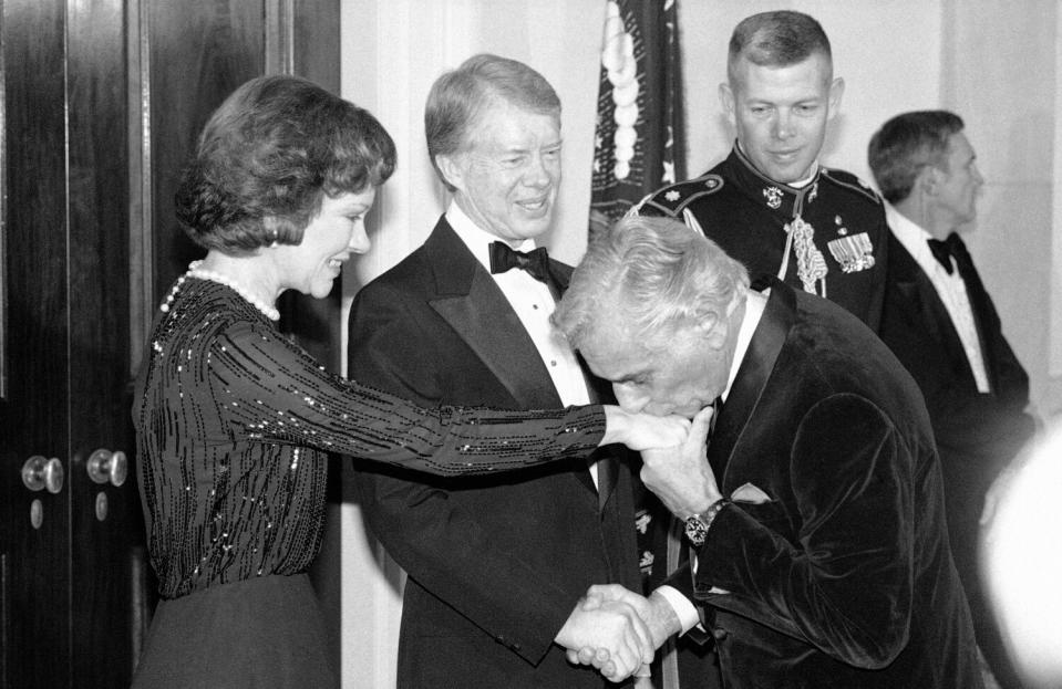 black and white photo of a man kissing a woman's hand with another in a tux standing by