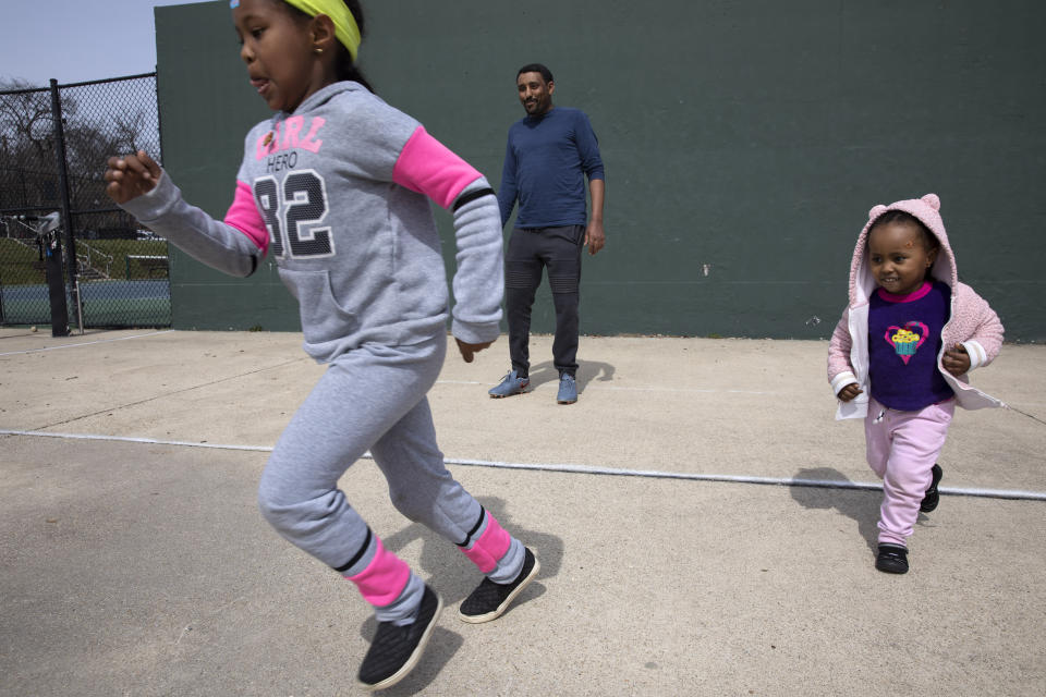 Aragaw Beyene, center, of Washington, plays with his cousins' children, Eldana Tilahune, 6, left, and Meklit Tilahune, 2, Monday, March 16, 2020, at a public park in northwest Washington. Beyene and his extended family are taking turns watching each other's children so the others can work while schools are closed due to coronavirus precautions. "I normally drive an Uber," says Beyene, "but it's scary to drive an Uber right now with the coronavirus. I haven't gone to work since Friday. Although I hear there is not much work." The family says they may stop taking the children to parks outside due to coronavirus fears. (AP Photo/Jacquelyn Martin)