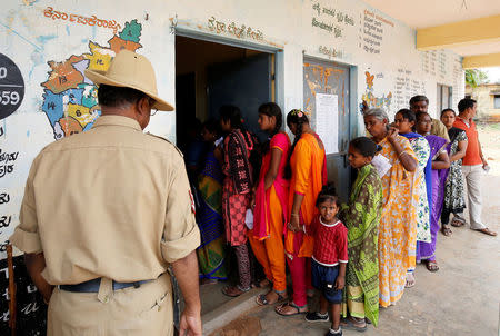 A policeman stands guard as voters wait in a queue to cast their ballot outside a polling station during Karnataka assembly elections at a village on the outskirts of Bengaluru, India, May 12, 2018. REUTERS/Abhishek N. Chinnappa