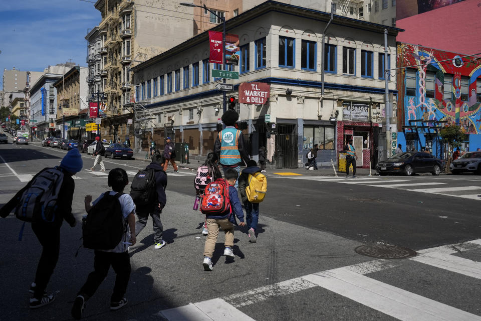 Children are escorted safely across an intersection in the Tenderloin neighborhood Wednesday, March 20, 2024, in San Francisco. (AP Photo/Godofredo A. Vásquez)