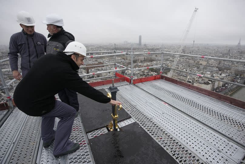 French President Emmanuel Macron (L) touches the top of the newly rebuilt spire and cross, during his visit to the reconstruction work at Notre-Dame de Paris Cathedral