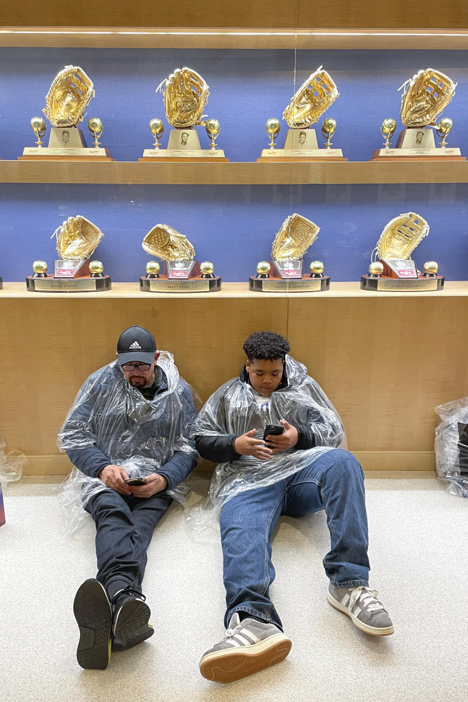 Fans wait in a lobby under Gold Gloves during a rain delay before a baseball game between the Los Angeles Dodgers and the San Diego Padres, Saturday, April 13, 2024, in Los Angeles. (AP Photo/Marcio Jose Sanchez)