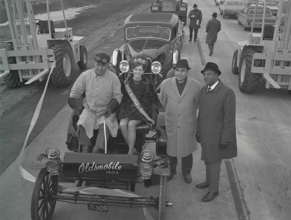 A 1904 Oldsmobile carrying Barbara Dean, Miss Michigan Highways of 1970, and driven by Bernie LaDuke, with an unidentified man and Dick Letts, far right, at the opening of the I-496 Oldsmobile Expressway, Dec. 18, 1970.