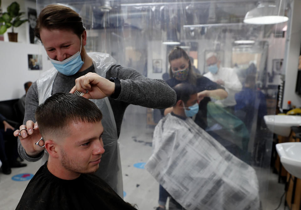 People get their hair cut at a busy hairdressers in London, Monday, April 12, 2021. Millions of people in England will get their first chance in months for haircuts, casual shopping and restaurant meals on Monday, as the government takes the next step on its lockdown-lifting road map.(AP Photo/Frank Augstein)