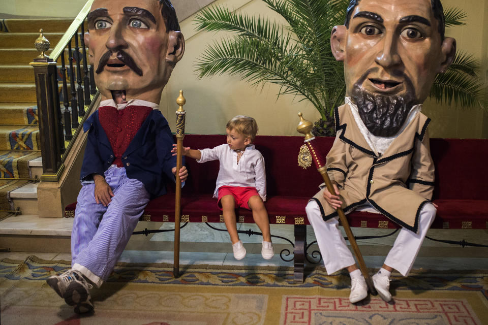 <p>A child sits next to a “cabezudo” and grabs his cane as they pause during a procession at the San Fermín Festival in Pamplona, Spain, July 14, 2015. (AP Photo/Andres Kudacki) </p>