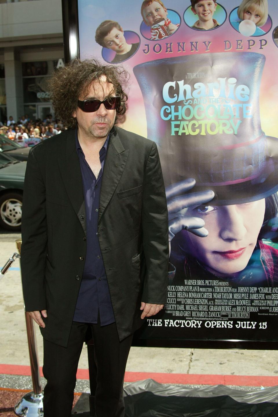 Tim Burton standing next to Charlie and the Chocolate Factory poster