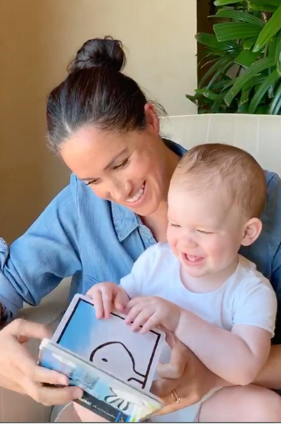 In this photo taken by Prince Harry, Duchess Meghan of Sussex reads "Duck! Rabbit!" to their son Archie who celebrated his first birthday May 6, 2020, in Los Angeles. She is wearing a chambray shirt.