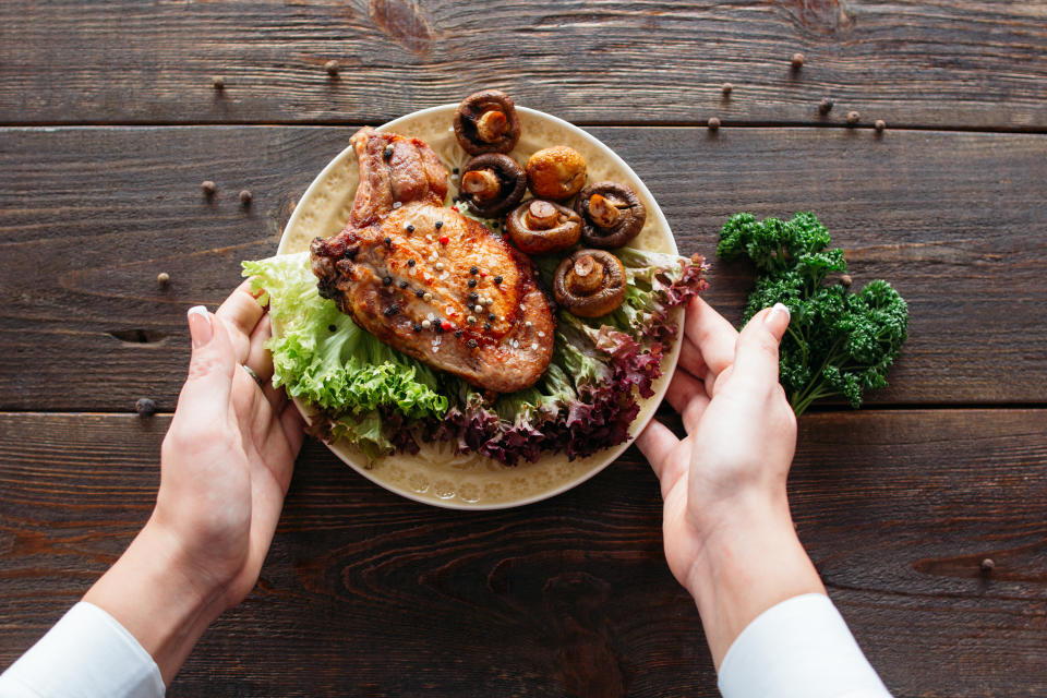 Waiter serving a chicken dish with lettuce and mushrooms. Chief decorating food for presentation in small cafe. Waiter presenting grilled chicken with salad for retail. (Getty Images)