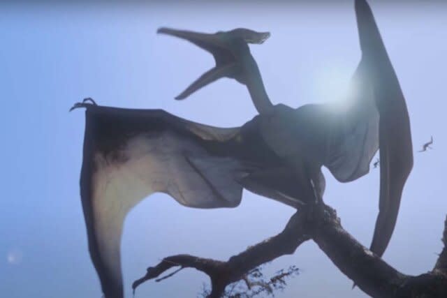 A backlit Pteranodon on a tree branch roars in the  Jurassic Park film series.