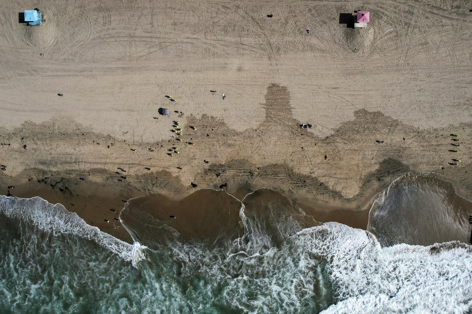 FILE - In an aerial photo take with a drone, workers in protective suits continue to clean an oil-contaminated beach in Huntington Beach, Calif., on Oct. 11, 2021. A Houston-based oil company on Monday sued two container ship operators and an organization that helps oversee marine traffic, saying they failed to prevent last fall's underwater pipeline leak off the Southern California coast. Amplify Energy Corp., which owns the pipeline that ruptured and faces a criminal charge for its oversight, claims that in January 2021 two ships dragged their anchors across the pipeline that ferried crude from offshore oil platforms to the coast. (AP Photo/Ringo H.W. Chiu, File)