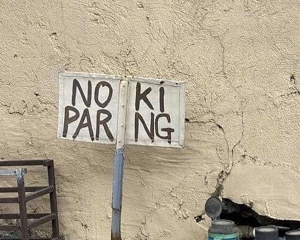 Handmade sign on a wall with the words "NO PARKING" split unevenly between two pieces of metal