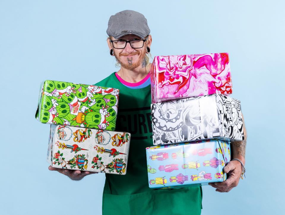 Curbside Chronicle vendor Steven holds packages wrapped in paper available through the OKC street paper's 2023 Wrap Up Homelessness program. Each package of wrapping paper features five different holiday designs from Oklahoma artists, printed locally on paper made in the United States.