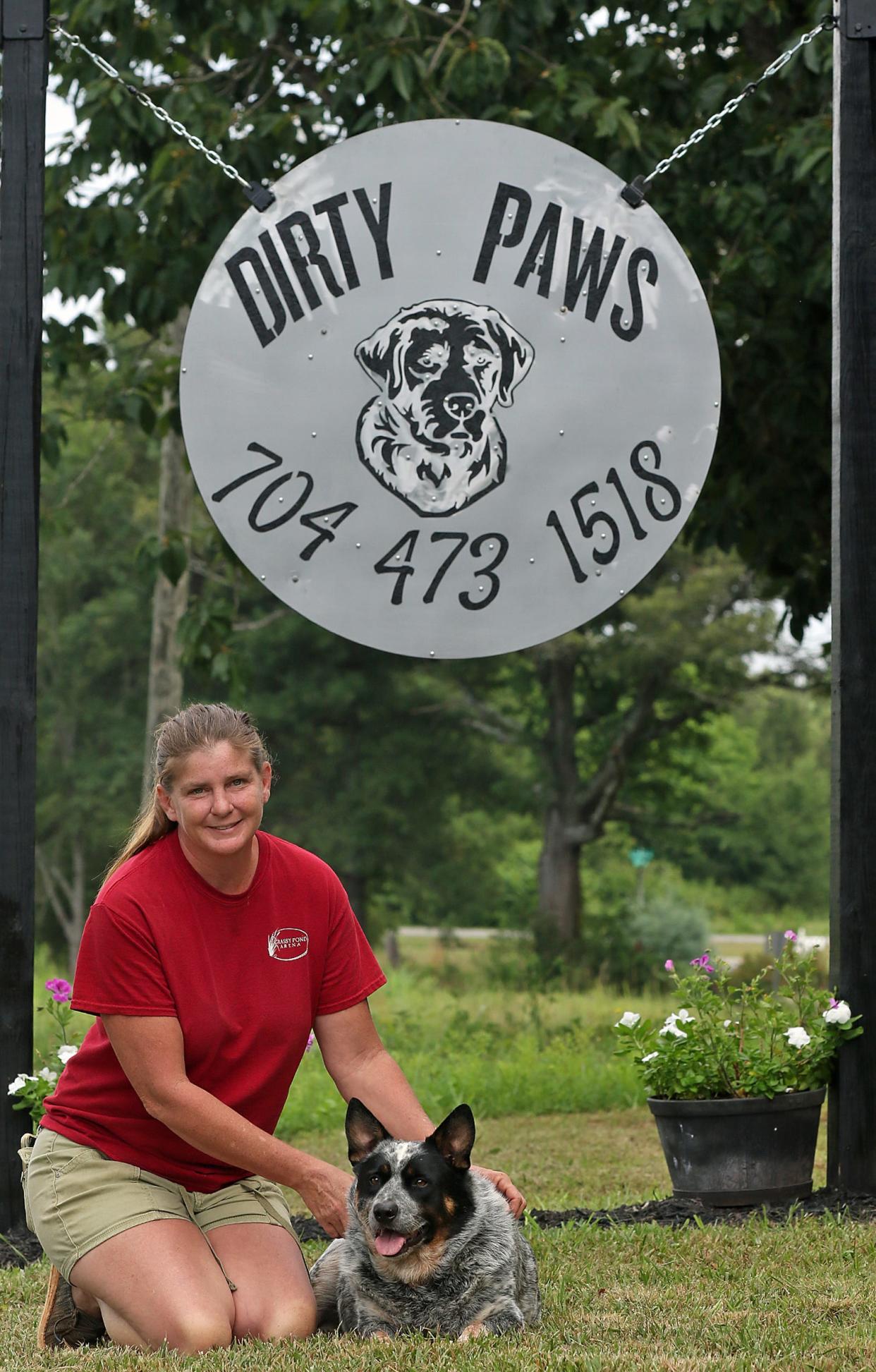 Owner Liza Jones and “Pepper” pose near the sign to Dirty Paws Salon on Steel Bridge Road near Mooresboro Monday morning, July 25, 2022.