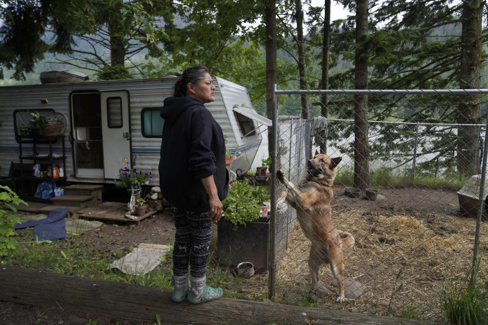 Sandy Whitefoot stands with a dog at her home on an "in-lieu fishing site," lands set aside by Congress to compensate tribes whose villages were inundated by dams, on Monday, June 20, 2022. Many families at these sites live in trailers without restrooms, lights or drains. (AP Photo/Jessie Wardarski)