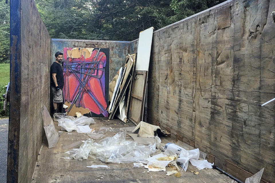 Jared Whipple stands next to a painting by Francis Hines found in a dumpster, Sept. 23, 2017, in Watertown, Conn. After fading into obscurity, Hines, who died in 2016, is again gaining attention after hundreds of his paintings were rescued by a car mechanic from a dumpster in Connecticut. An exhibit of that art will open May 5, 2022, at the Hollis Taggart galley in Southport, which is known for showing the works of lost or forgotten artists. (Scott Whipple via AP)