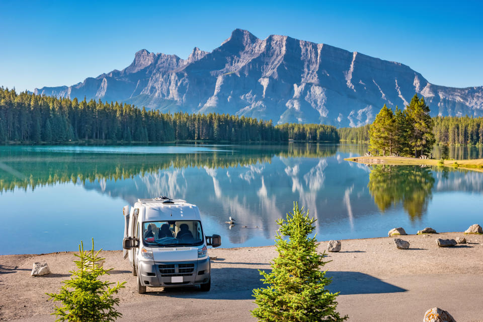 Campervan parked on a lake with tall trees and mountain behind it