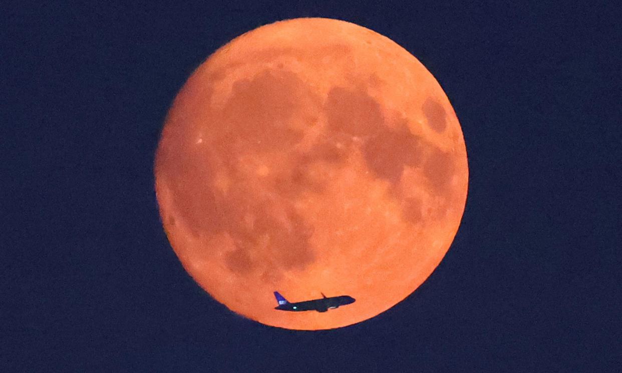 <span>An aircraft passes in front of the moon over London on Sunday night. The moon has an orange hue due to wildfires in North America.</span><span>Photograph: Toby Melville/Reuters</span>