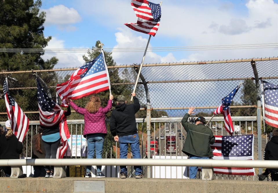 About 30 people display flags and waved at truckers from an Interstate 5 overpass on Tuesday, Feb. 22, 2022, in Redding during a rally to support the cross-country People's Convoy. An estimated 1,000 semi-truck drivers are expected on Wednesday to descend on Adelanto, the official starting point of the cross-country convoy to protest government COVID-19 mandates.