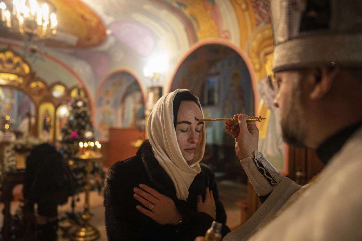 An Orthodox priest offers the holy communion to a woman during Christmas church service in Kostyantynivka, Ukraine, Friday, Jan. 6, 2023. (AP Photo/Evgeniy Maloletka)