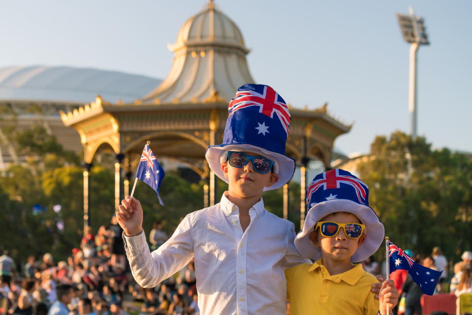 Two children wearing Australian flag hats, hold up Australian flags.