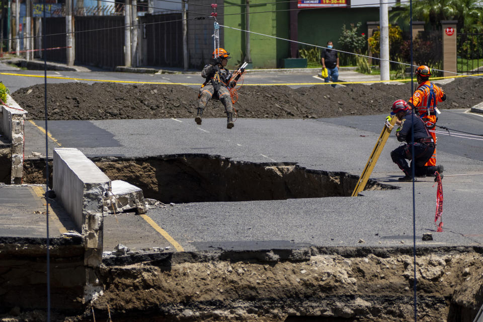 Rescuers of the Guatemalan Army descend into a sinkhole in Villa Nueva, Guatemala, Tuesday, Sept. 27, 2022. Search efforts were underway for a mother and daughter who disappeared when their vehicle was swallowed by a massive sinkhole. (AP Photo/Moises Castillo)