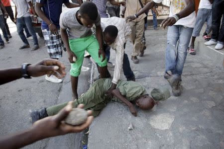 A man kicks in the head of an unidentified man in military style clothes who was stoned to death by a mob of protesters in Port-au-Prince, Haiti, February 5, 2016. REUTERS/Andres Martinez Casares