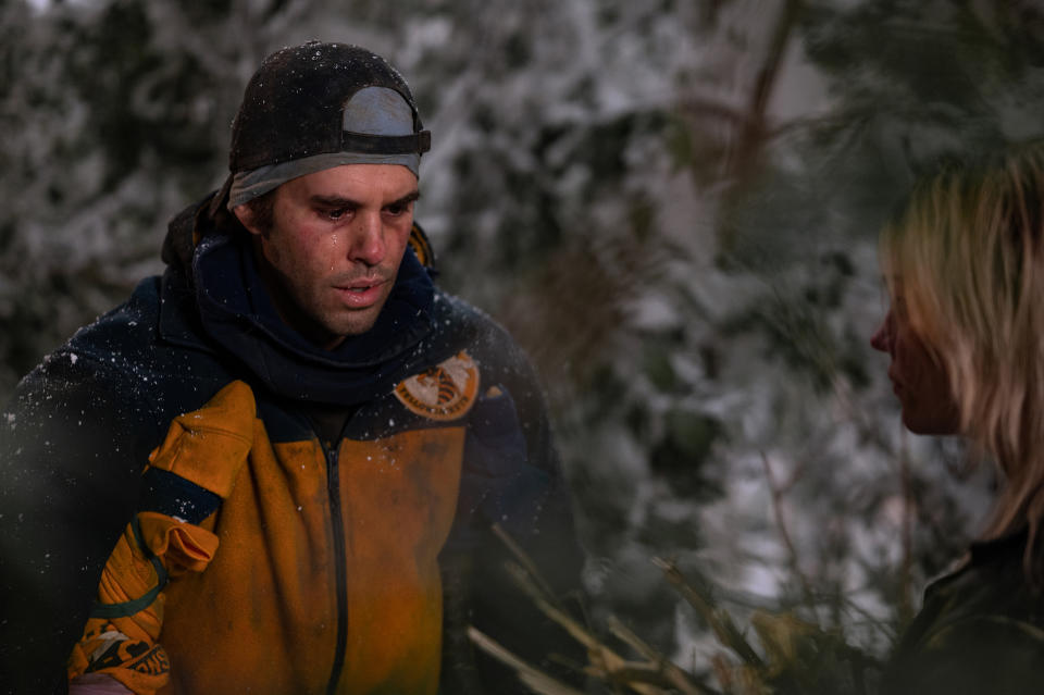 A man in a yellow and navy blue athletic jacket and backward baseball cap, crying as he stands on a crutch outside in the snow; still from "Yellowjackets"