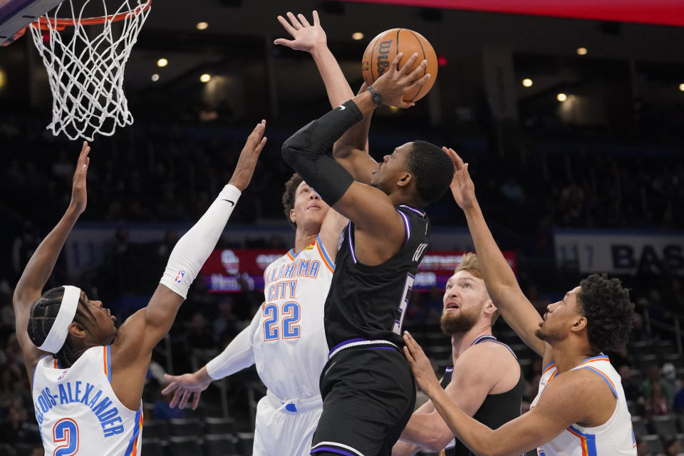 Sacramento Kings guard De'Aaron Fox (5) shoots between Oklahoma City Thunder guard Shai Gilgeous-Alexander (2), forward Isaiah Roby (22) and guard Aaron Wiggins, right, in the first half of an NBA basketball game Monday, Feb. 28, 2022, in Oklahoma City. (AP Photo/Sue Ogrocki)