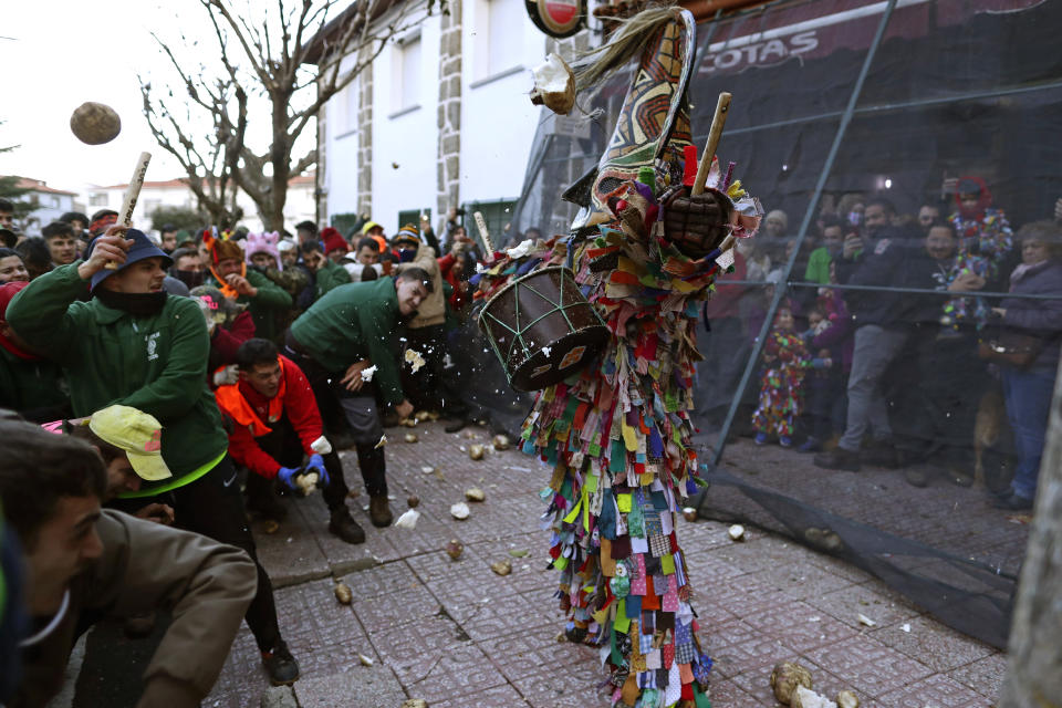 In this photo taken on Sunday, Jan. 19, 2020, people throw turnips at the Jarramplas as he makes his way through the streets beating his drum during the Jarramplas festival in the tiny southwestern Spanish town of Piornal, Spain. The Jarramplas festival features a man in multicolored garb and pointy wooden headgear to shield himself from turnips. A crowd of men in the street pelt the man with the vegetables from close range at the fiesta held annually at Piornal, 200 kilometers west of Madrid, over two days. (AP Photo/Manu Fernandez)