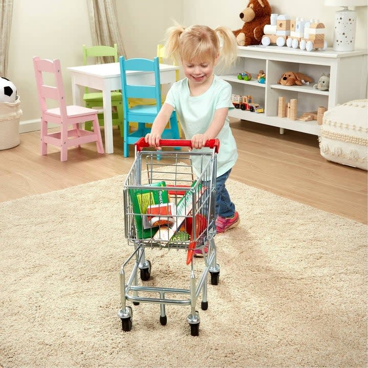 Young girl pushing a metal shopping cart full of pretend food