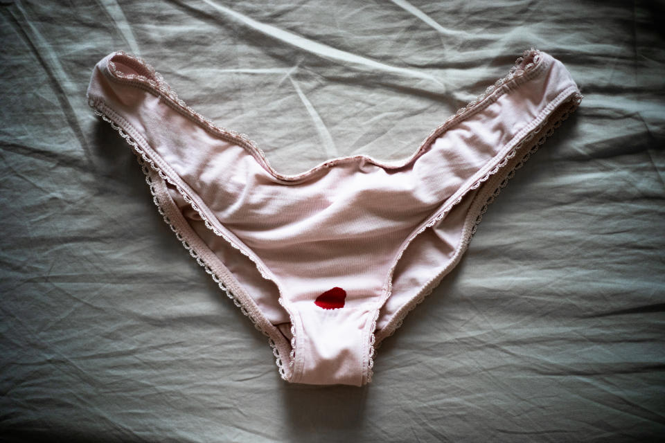 Menstruation blood stain on pink panties lying on a bed with grey sheets